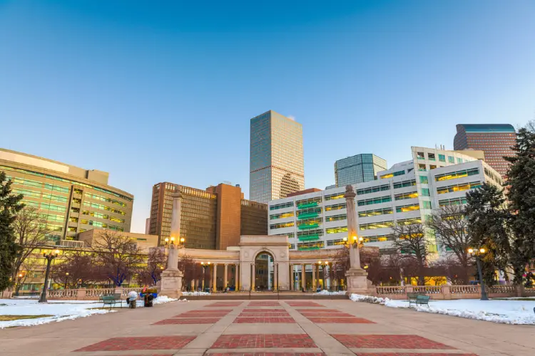 View of downtown Denver skyline with Civic Center architecture, office towers, and public plaza at sunset.