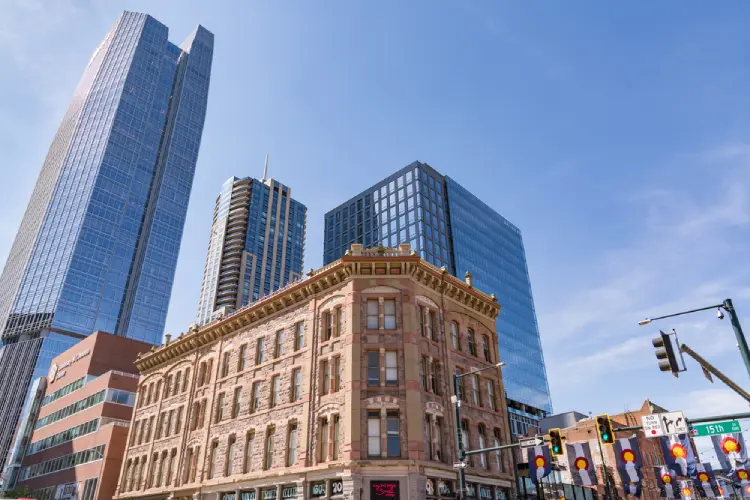 Historic brick building in LoDo Denver with modern glass skyscrapers rising in the background on a sunny day.