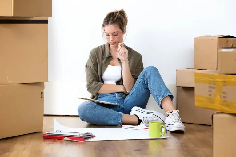 Woman sitting on floor with moving boxes and clipboard, preparing a checklist to stay organized on Denver high-rise moving day.