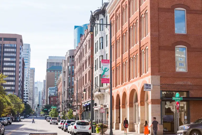 Downtown Denver street with cars parked along buildings, representing the need for right-of-way signage and parking permits during high-rise moves.